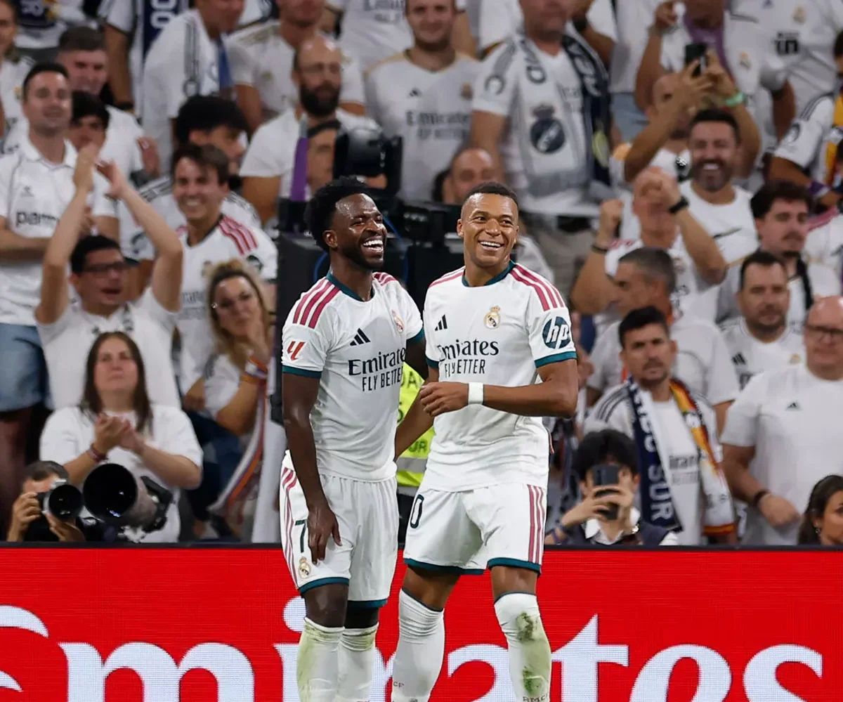 Vinícius Júnior and Kylian Mbappé smiling during a Real Madrid goal celebration